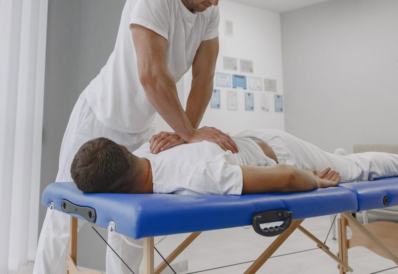 Man in the medical office. Physiotherapist is rehabilitating back.